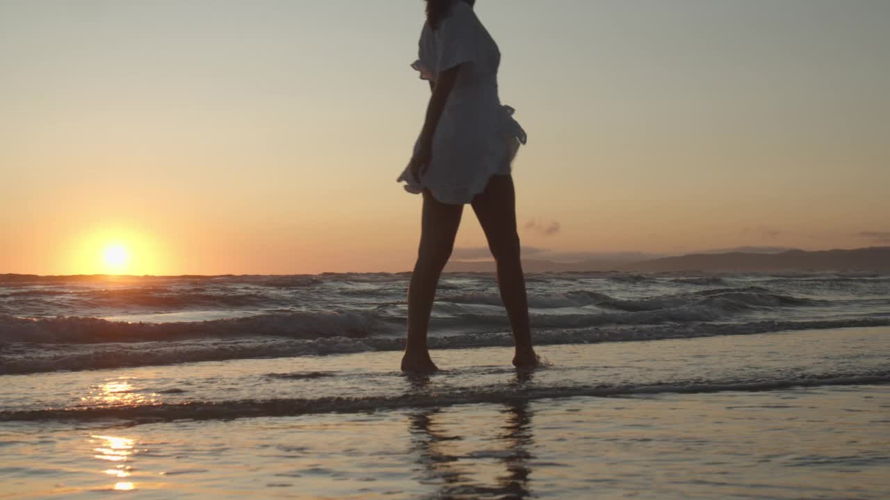 夕阳西下，身着白裙的女子在大海中漫步视频素材