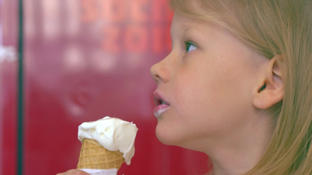 美丽的金发小女孩吃着冰淇淋，环顾四周，笑着视频素材