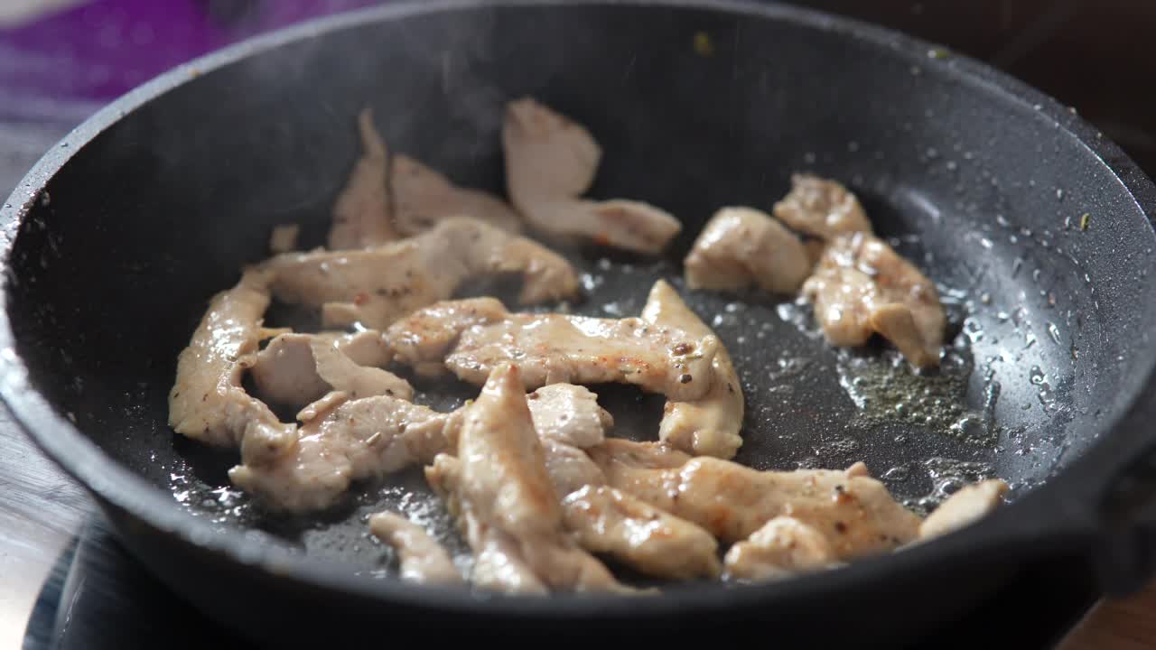 把肉块放在煎锅里煎。在煎锅中用热油煎鸡肉，特写。视频素材