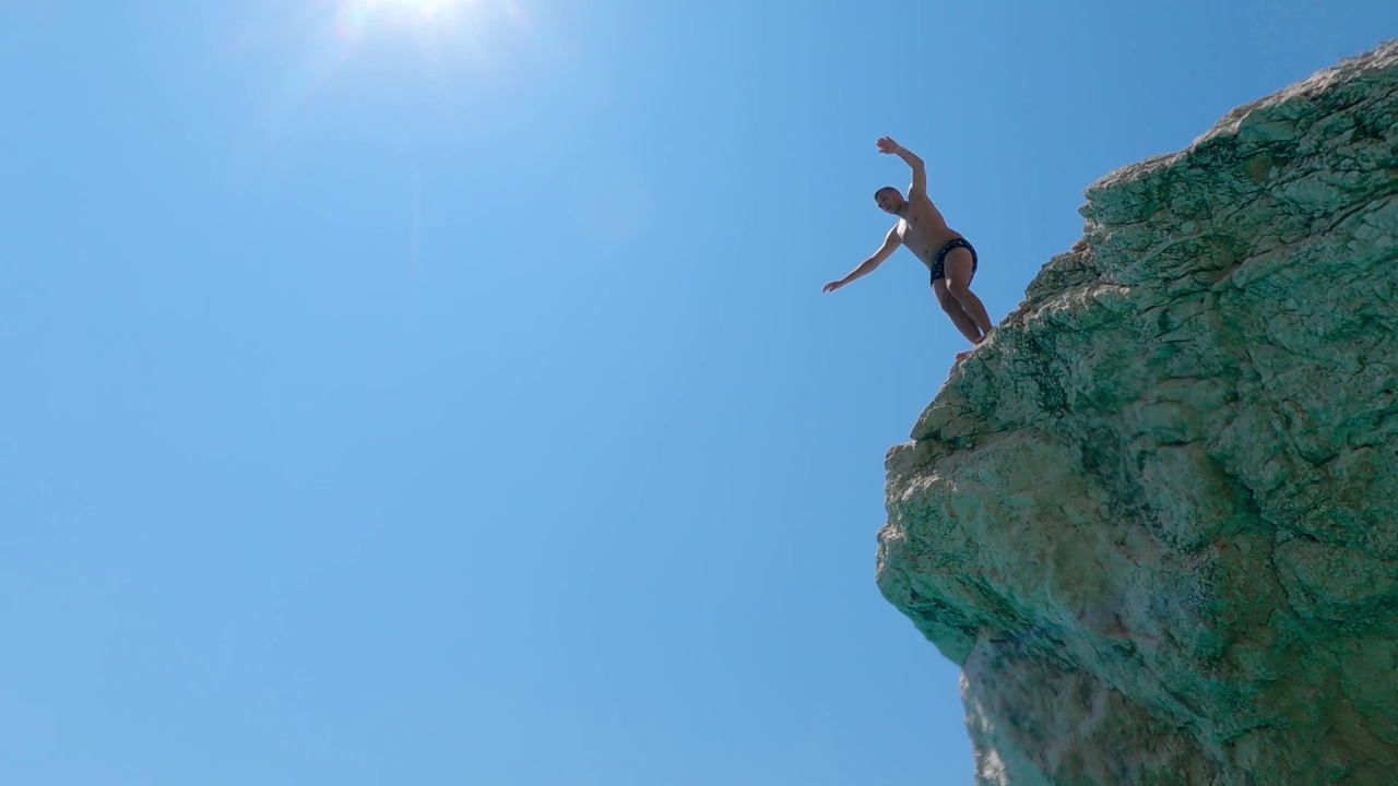 肾上腺素头跳。在希腊莱夫卡达的凯西斯玛海滩上，一个年轻人在碧绿的海水中跳跃，慢镜头视频下载