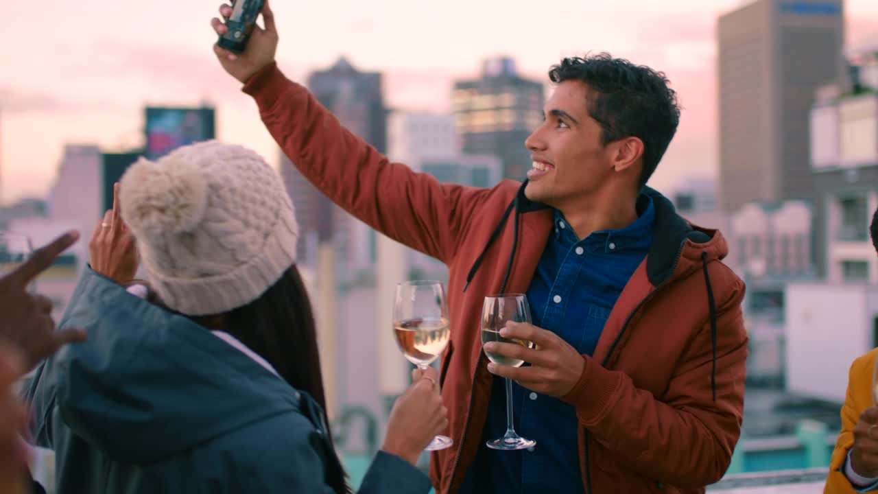 社交媒体上的朋友，庆祝和在智能手机上的屋顶派对的自拍，集体在日落喝酒的乐趣。快乐的人们举杯，庆祝活动成功，微笑着拍下城市屋顶的照片视频下载