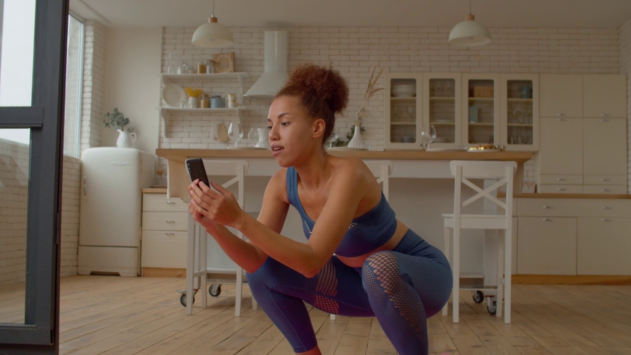 多任务运动适合黑人女性与手机做深蹲锻炼视频下载