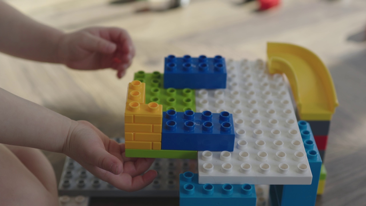 蹒跚学步的儿童用手、手指用鲜艳的彩色砖块建造建筑视频下载