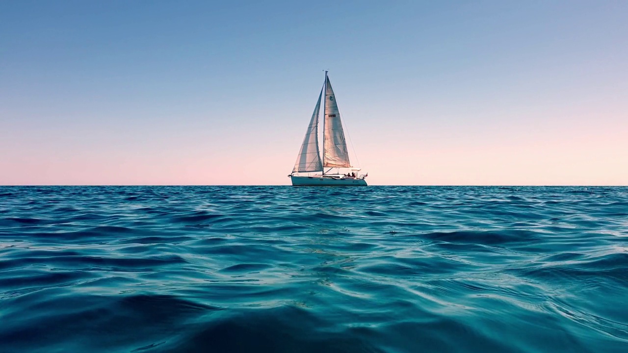 日落时，小游艇在平静的公海上航行的慢动作和低角度海平面视图视频素材