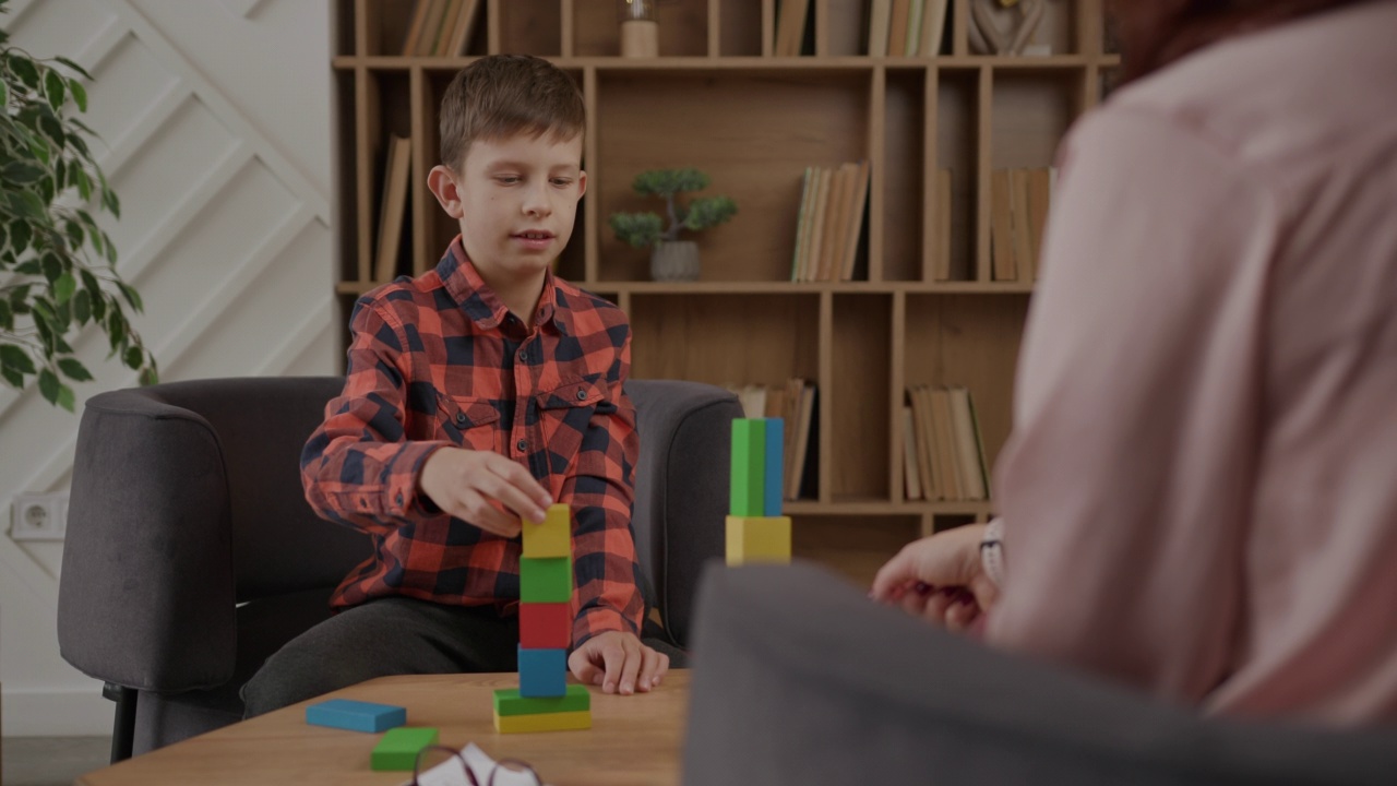 自闭症儿童用彩色积木搭起大楼坐在治疗师办公室里。自闭症谱系障碍教育。视频下载