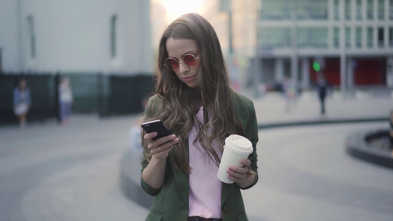 迷人的年轻女子带着咖啡，用着她的智能手机视频素材