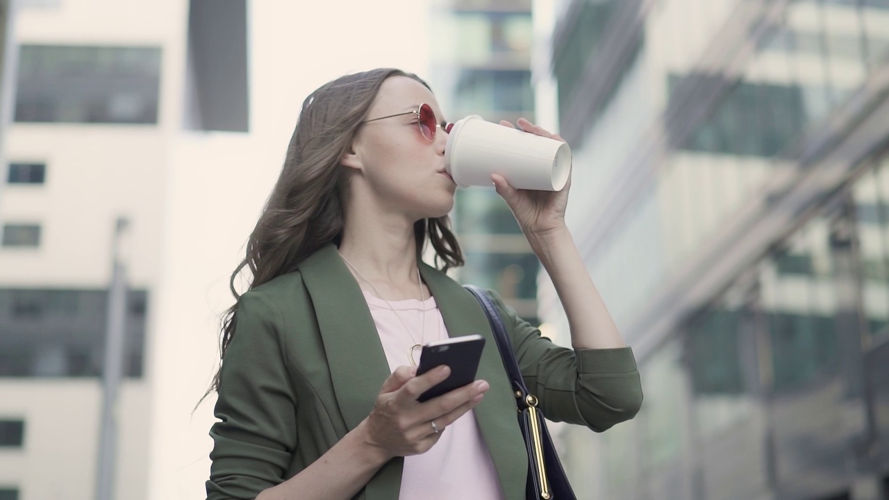 女人站在秋天的城市街道上网冲浪和喝咖啡视频素材