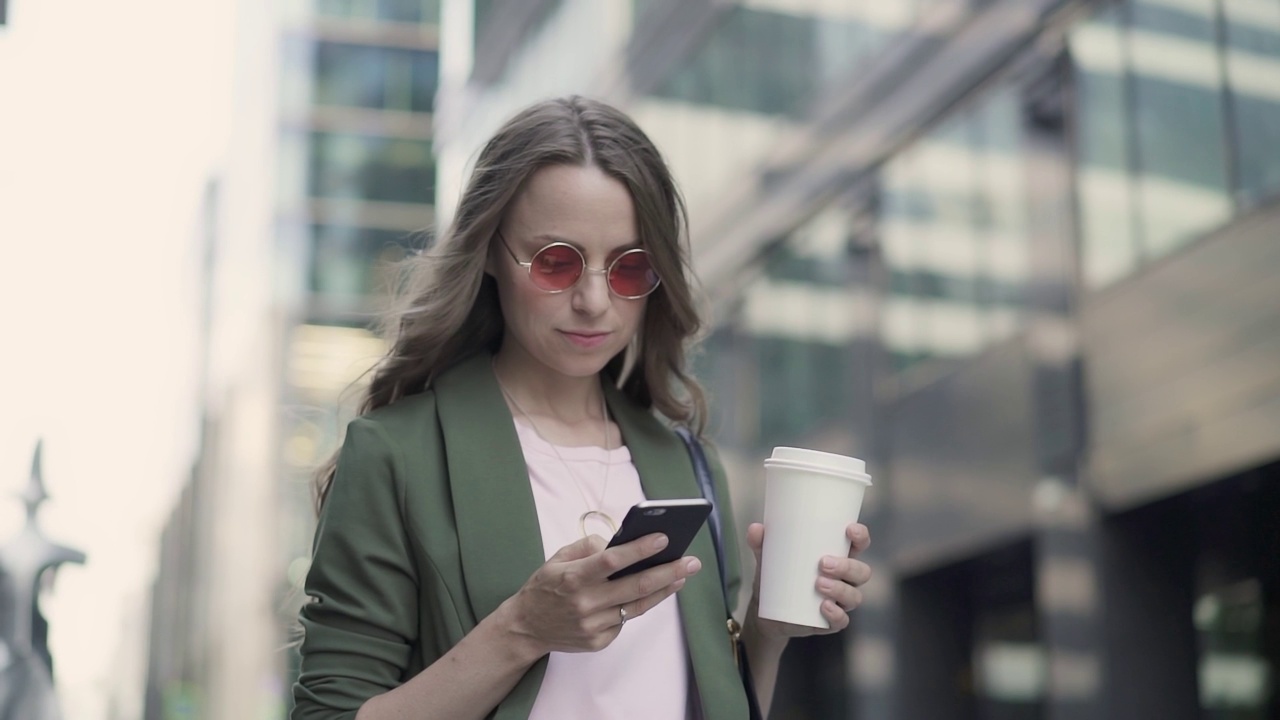 站在城市街道上的女人一边喝着咖啡一边上网冲浪视频素材