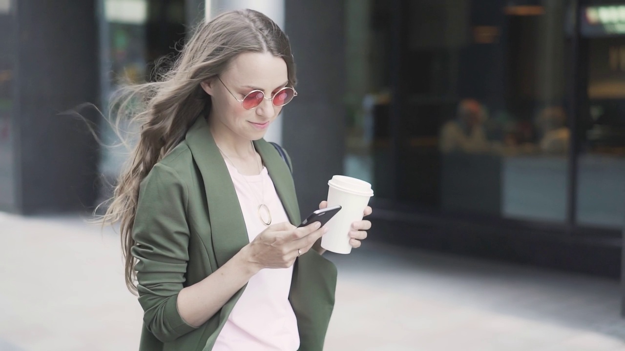 美丽的年轻女子拿着咖啡去网上冲浪走在街上视频素材