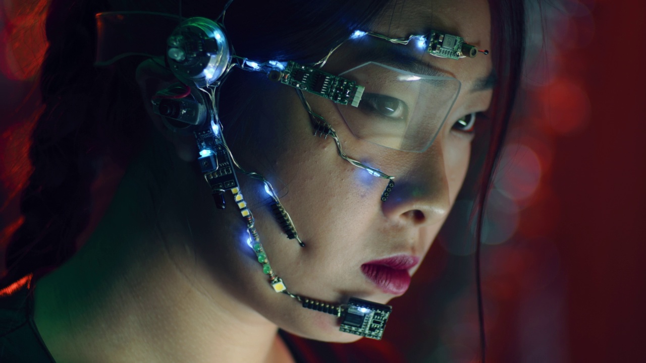 专注的亚洲女孩穿着赛博朋克服装，戴着未来主义眼镜在电脑上工作视频素材