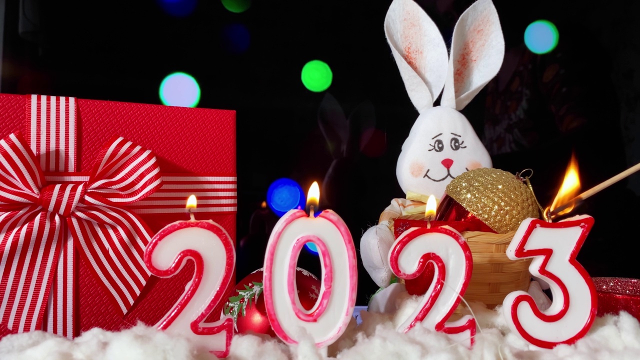2023年新年快乐。蜡烛和白色的兔子在黑色的节日闪闪发光的背景制作的2023。视频下载