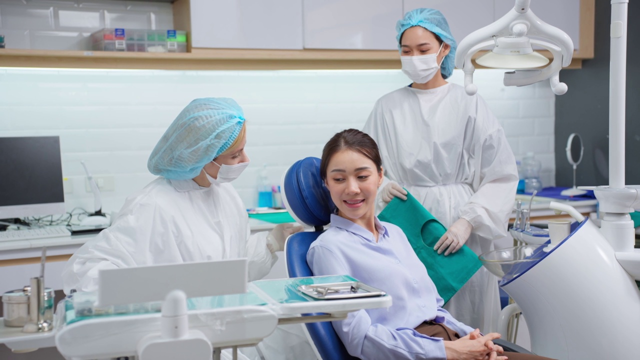 女牙医在牙科诊所为年轻的亚洲女孩检查牙齿。漂亮的女病人躺在牙科椅上，在医院预约手术时接受医生的牙科治疗。视频下载