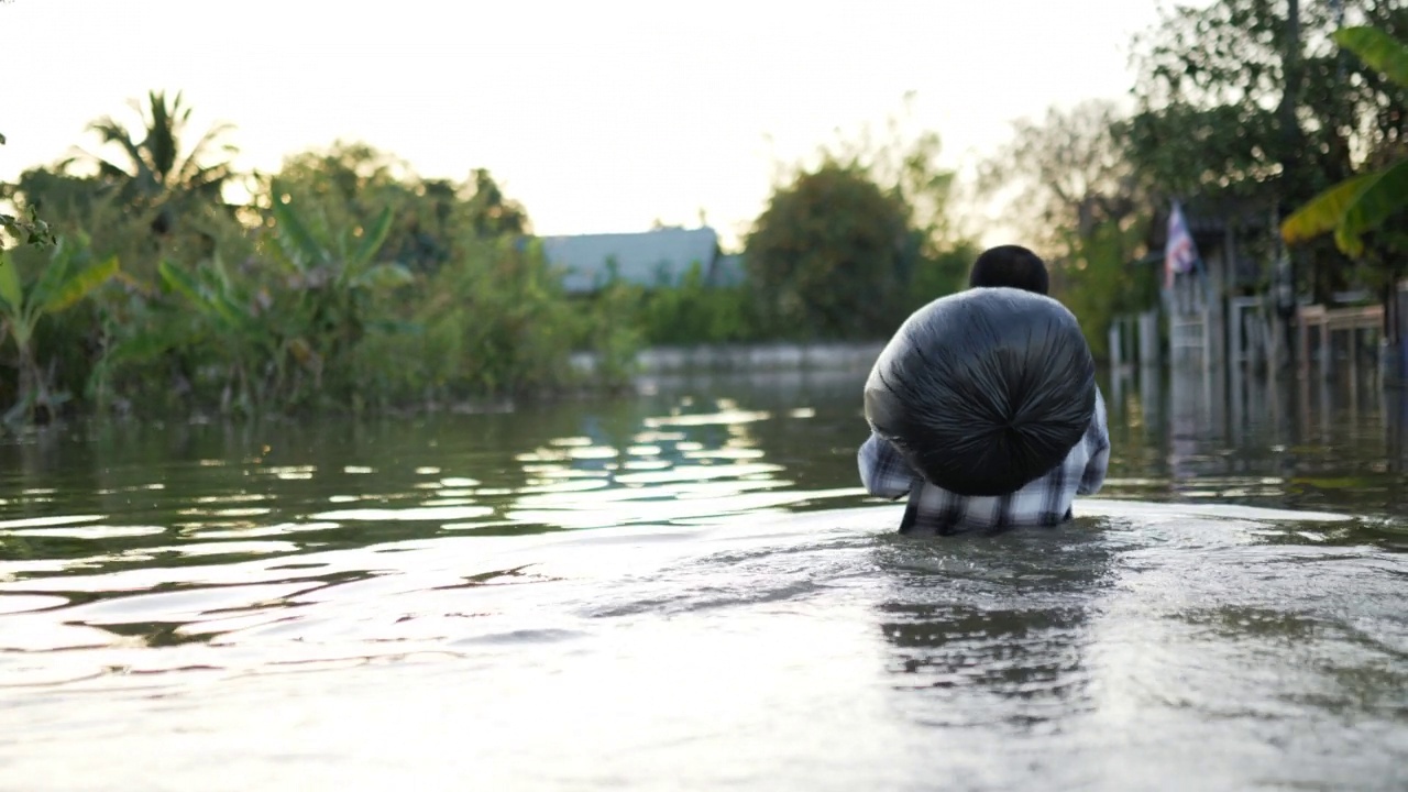 年轻人肩上扛着黑色塑料袋走在洪水中视频素材