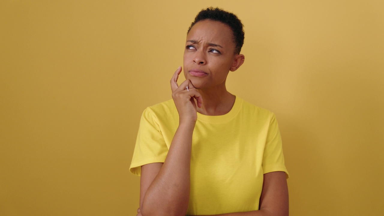 一名非洲裔美国妇女站在孤立的黄色背景下，带着怀疑的表情视频下载
