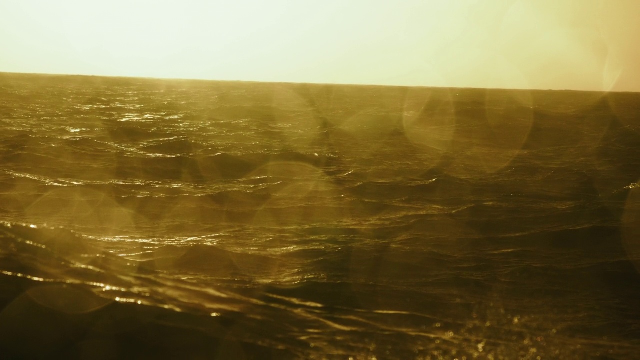 夕阳落在波涛汹涌的海面上，从一艘小船上驶过开阔的大海视频素材