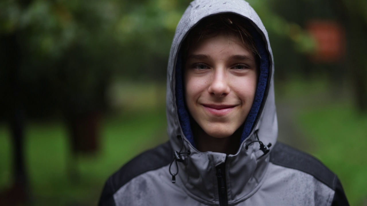 一个十几岁的男孩在一个秋雨天的公园里的画像。视频下载