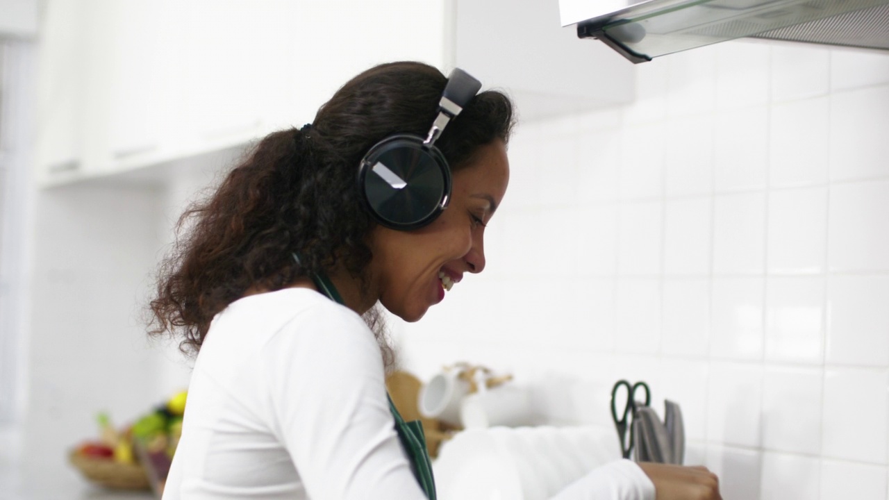 年轻女子在家里的厨房里做饭，同时戴着耳机听音乐视频素材