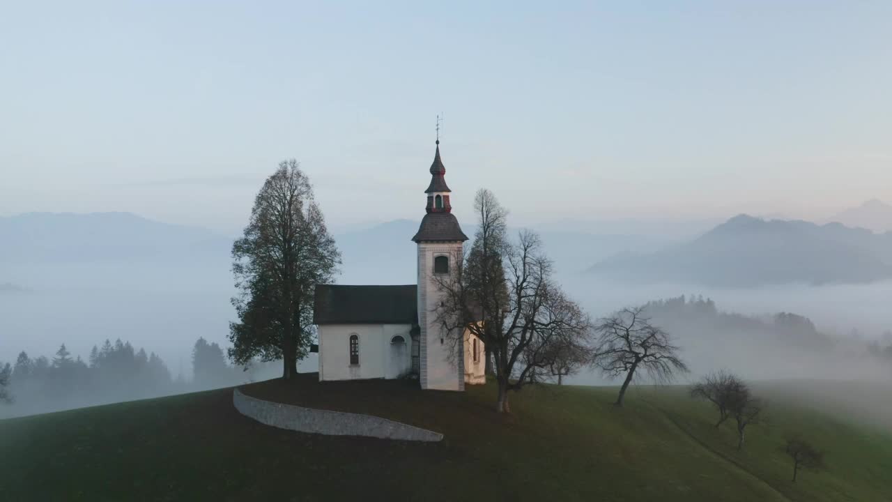 美丽的秋天雾蒙蒙的风景在日出俯视图。拂晓时分，在斯洛文尼亚的一座山上，在雾中绕着美丽的小教堂盘旋视频素材