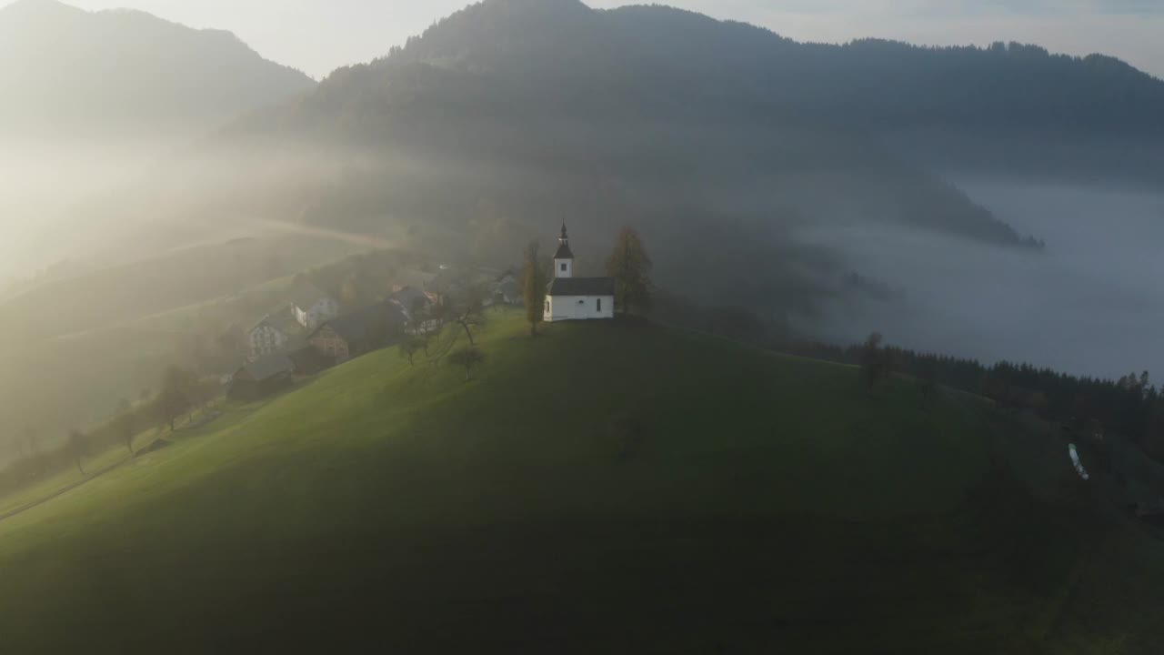 美丽的秋天雾蒙蒙的风景在日出俯视图。拂晓时分，在斯洛文尼亚的一座山上，在雾中绕着美丽的小教堂盘旋视频下载