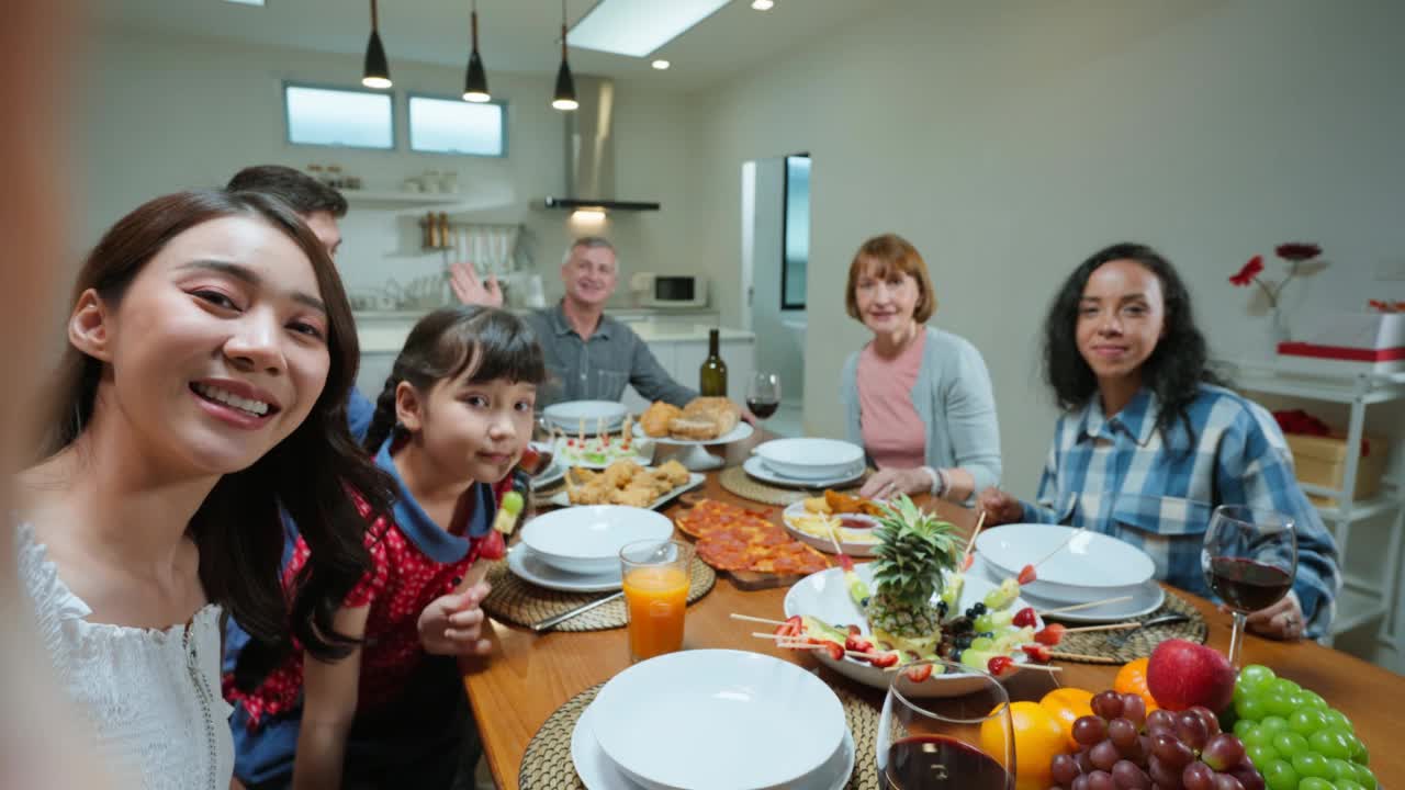 多民族家庭在家里聚餐时自拍。有吸引力的一群不同的人在家里的餐桌上欢聚一堂，吃着美食，庆祝周末团聚。视频下载