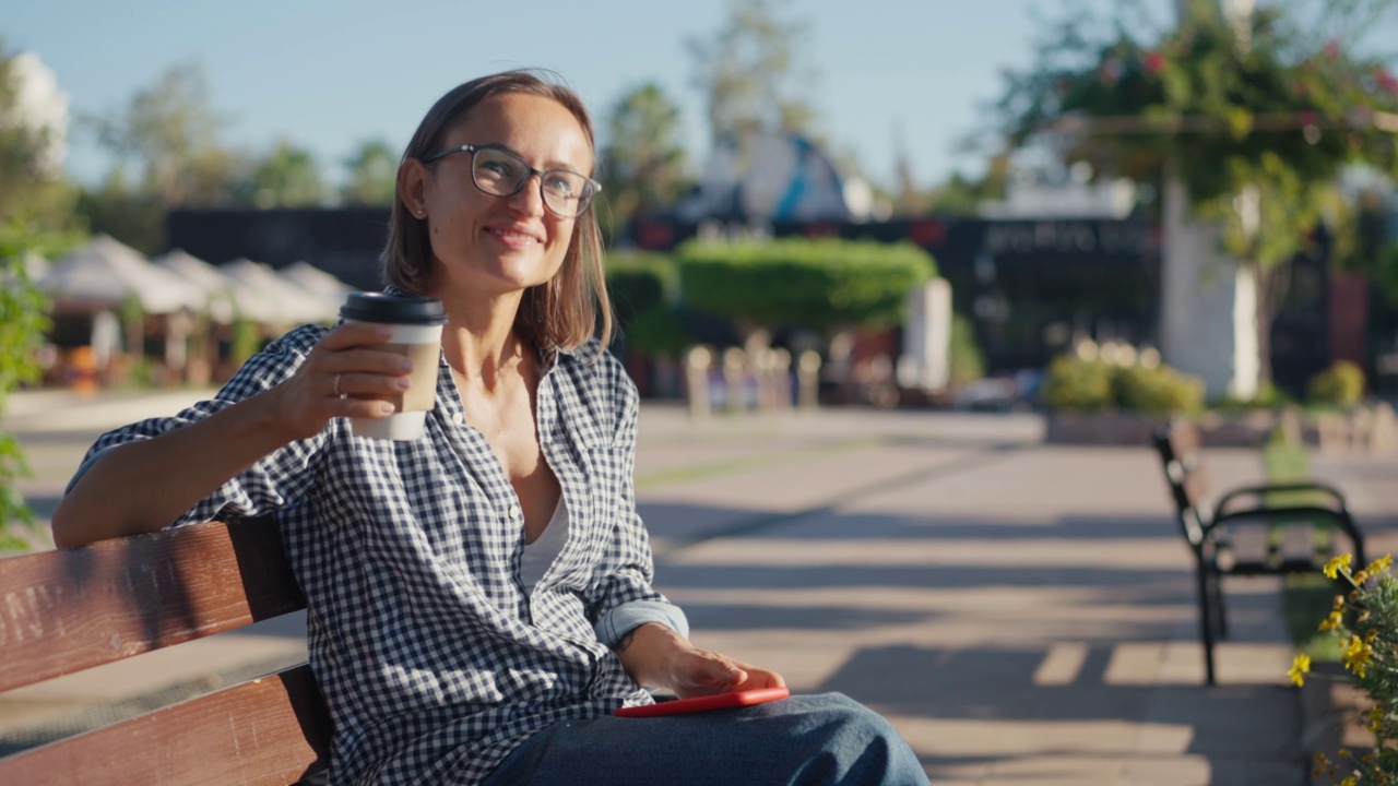 公园里的年轻女子拿着平板电脑和外卖咖啡视频素材