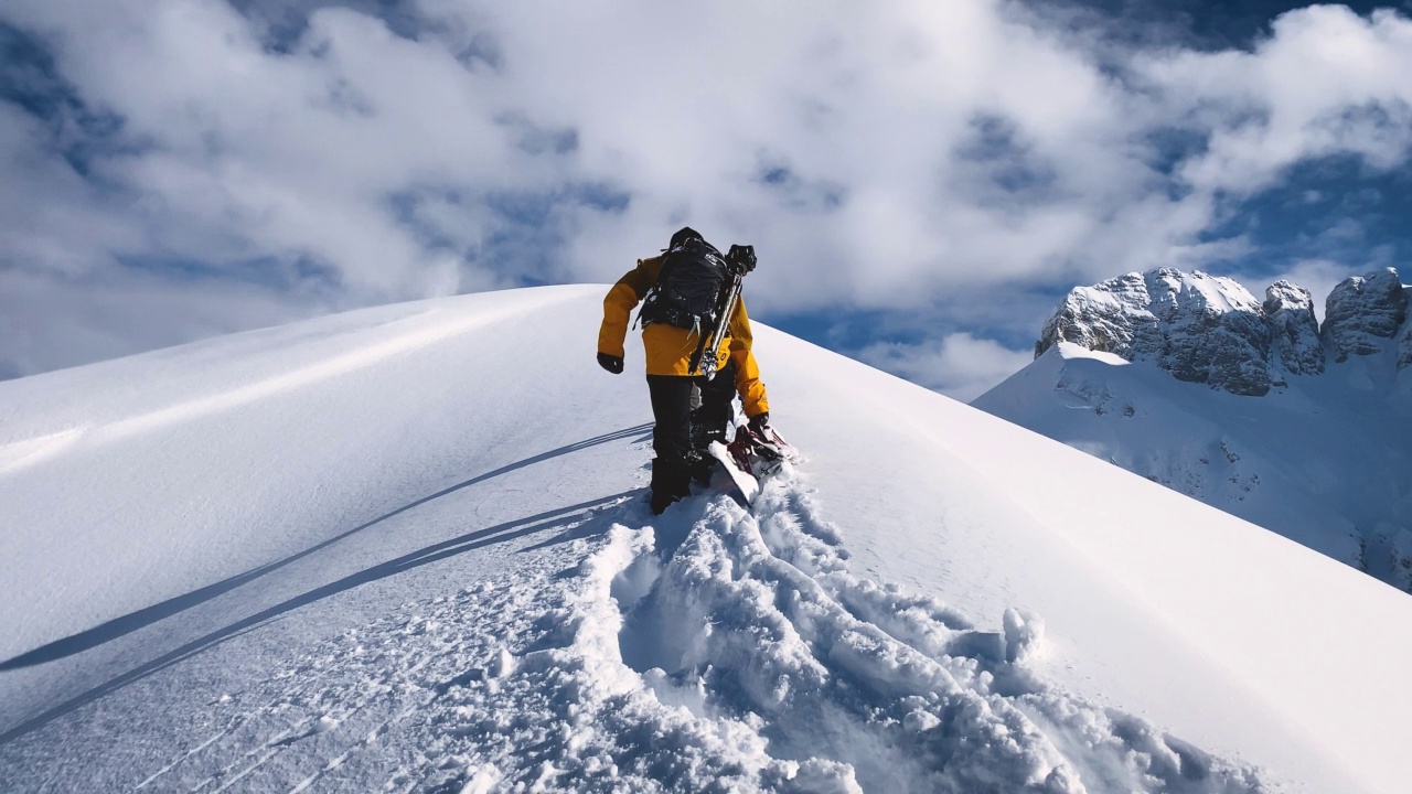 在山上厚厚的积雪中爬山的滑雪者视频素材