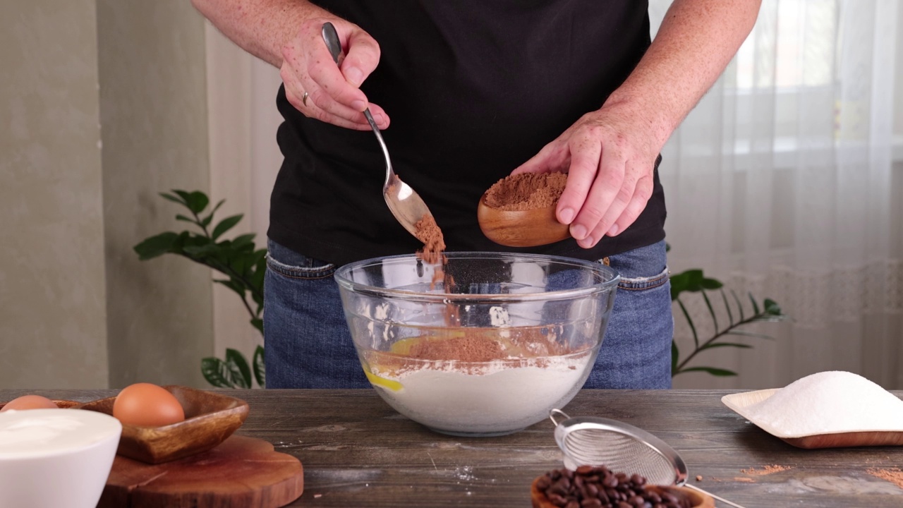 一名男子在做蛋糕时，把可可和糖倒在一碗面粉里视频素材
