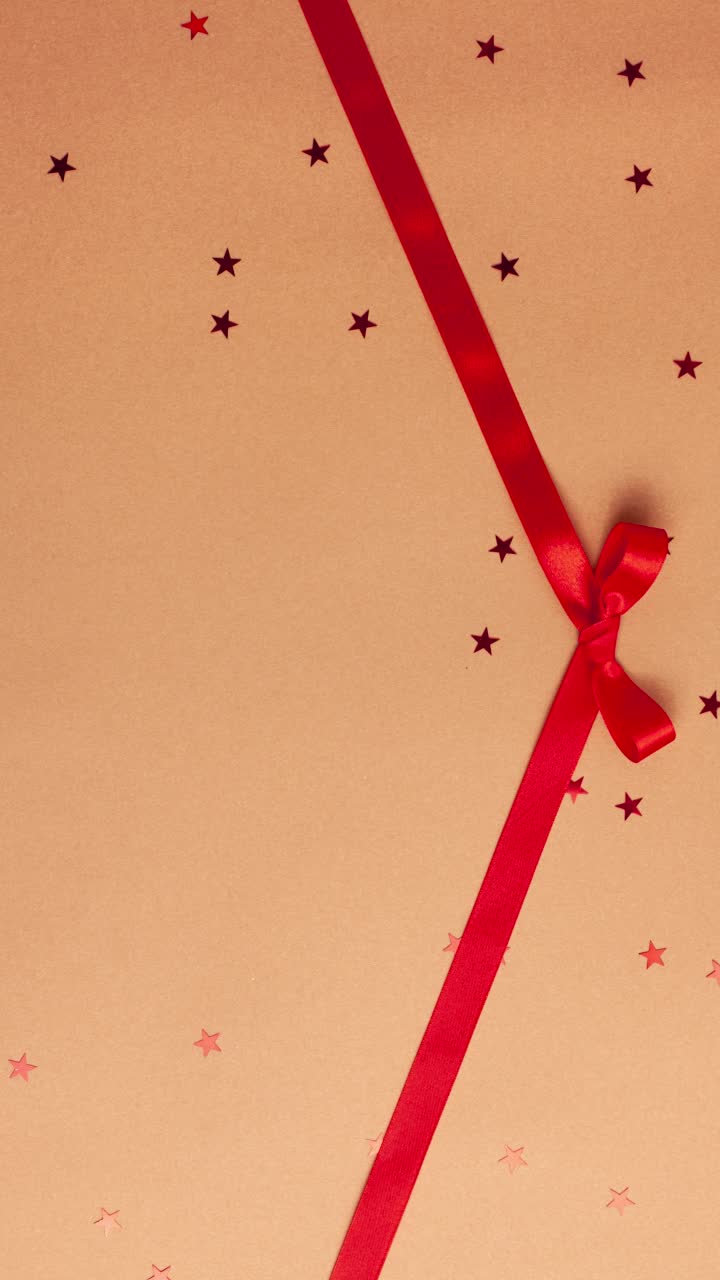 红色缎带蝴蝶结，在棕色的背景和红色的星星形状。定格动画垂直圣诞假期和呈现概念平面铺设与复制空间视频下载