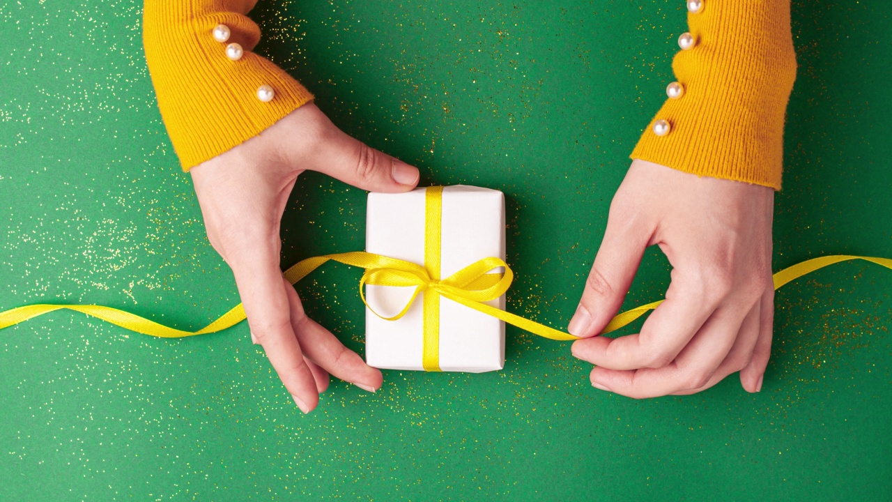 人类的手系一个黄色缎带蝴蝶结白色礼盒玉绿色背景与金色闪光。定格动画圣诞假期和现在的概念平铺视频下载