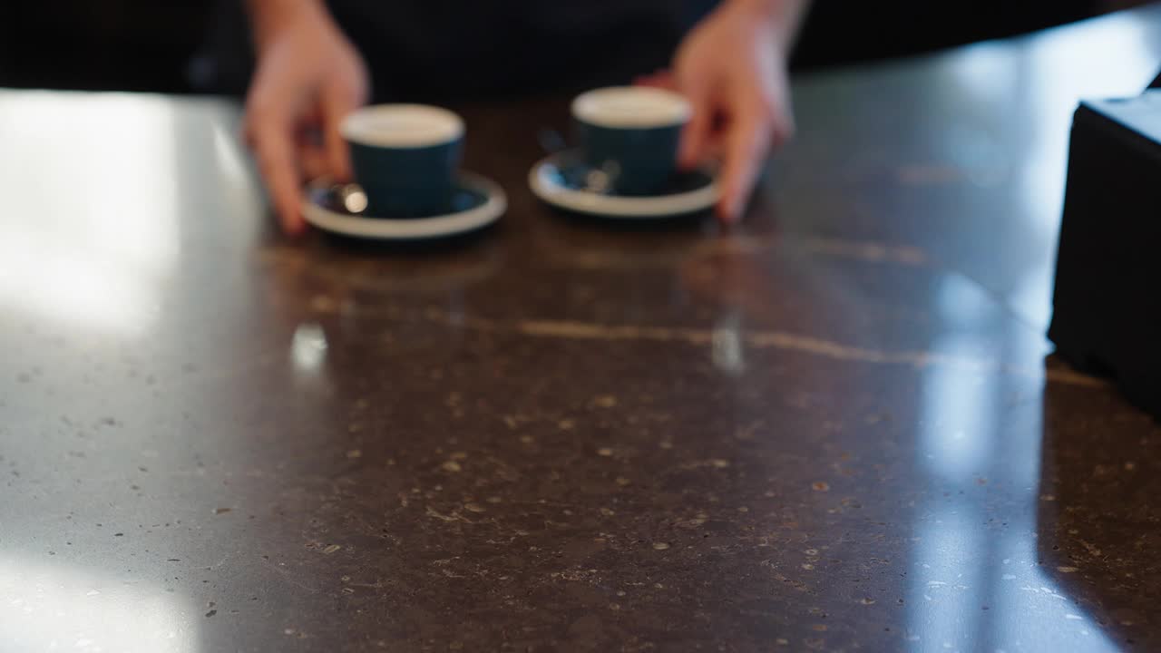 一个咖啡师在咖啡馆里提供两个热咖啡杯的特写视频素材