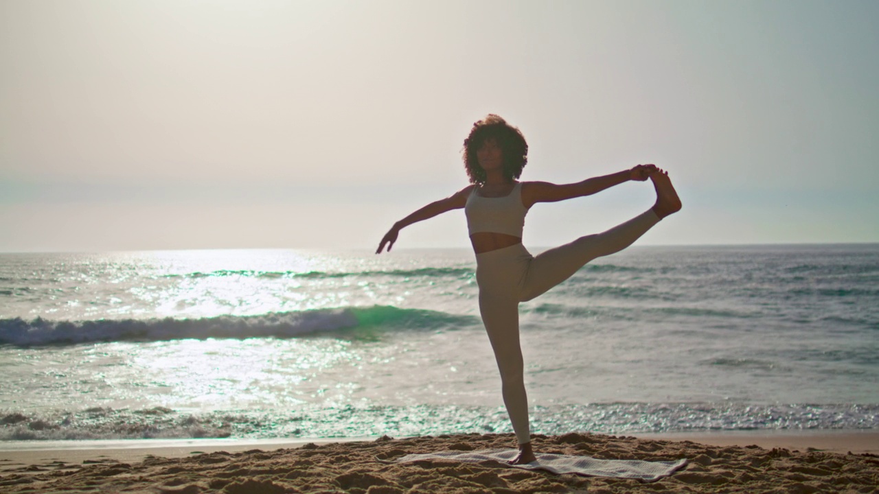 女子在日出时在海滩上练习姿势平衡。女孩单腿站立。视频下载