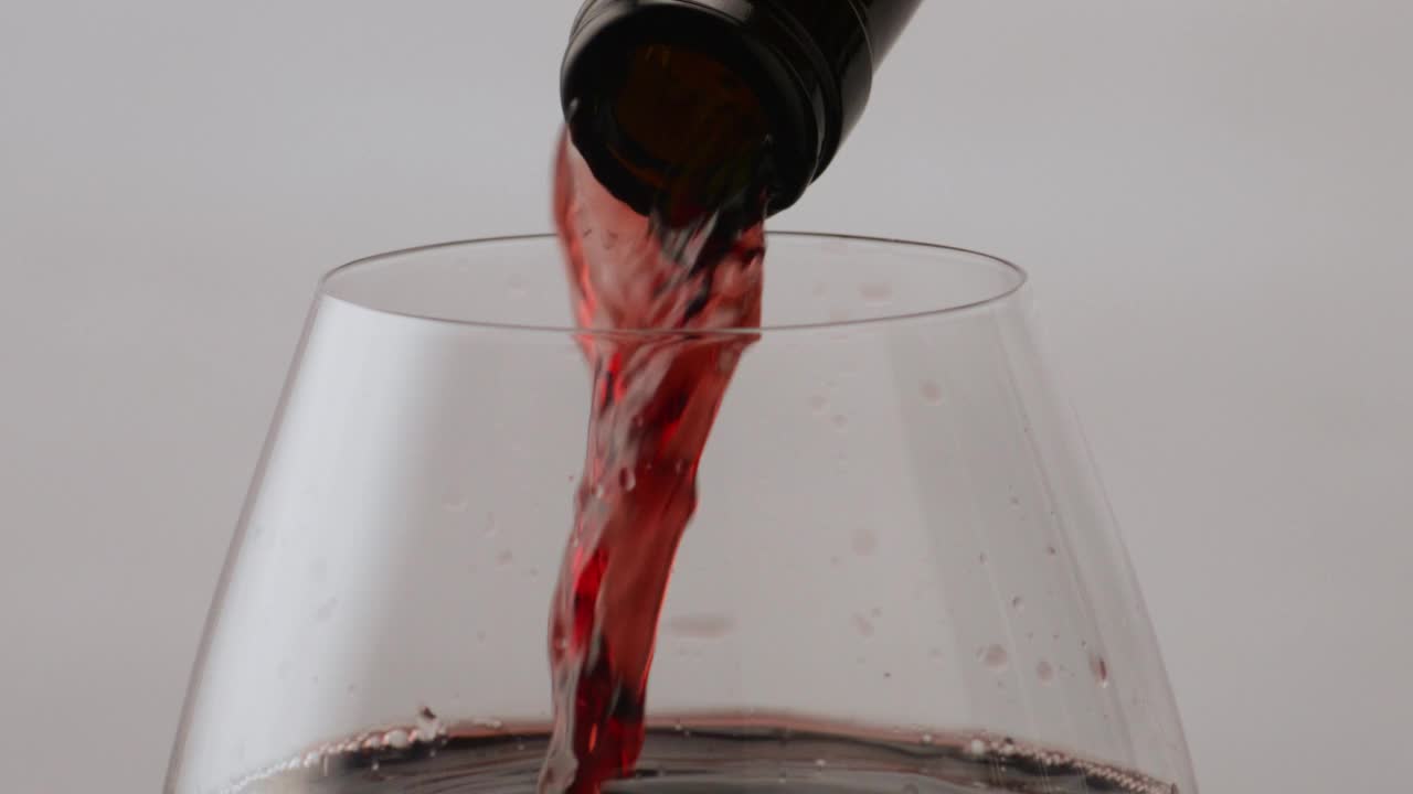 红酒从酒瓶中喷入高脚杯。流勃艮第酒。视频下载