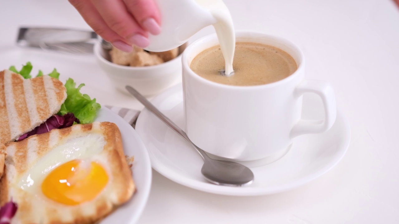 将咖啡奶油倒入一杯黑咖啡-美味的早餐-煎蛋，蘑菇和吐司视频下载