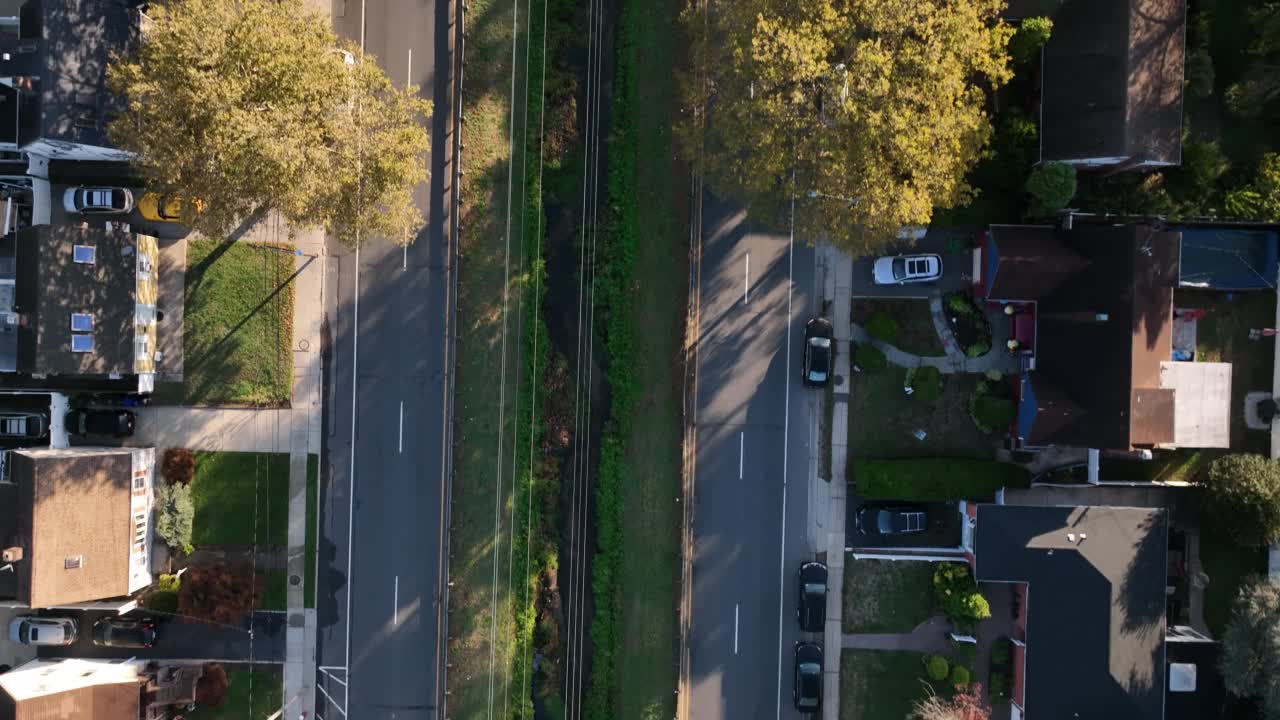 在一个阳光明媚的日子里，长岛一个绿色郊区街道上的汽车鸟瞰图视频素材