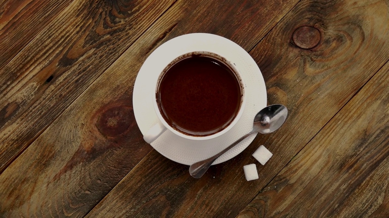 白色杯黑咖啡在茶碟上，茶匙和淋过的糖在深色木桌上旋转。视频下载