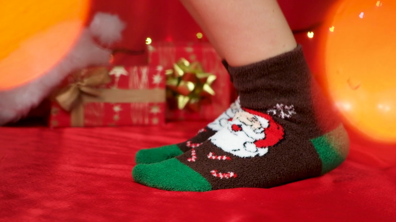 穿着圣诞袜的脚和圣诞老人在红色的除夕背景上跳。视频下载