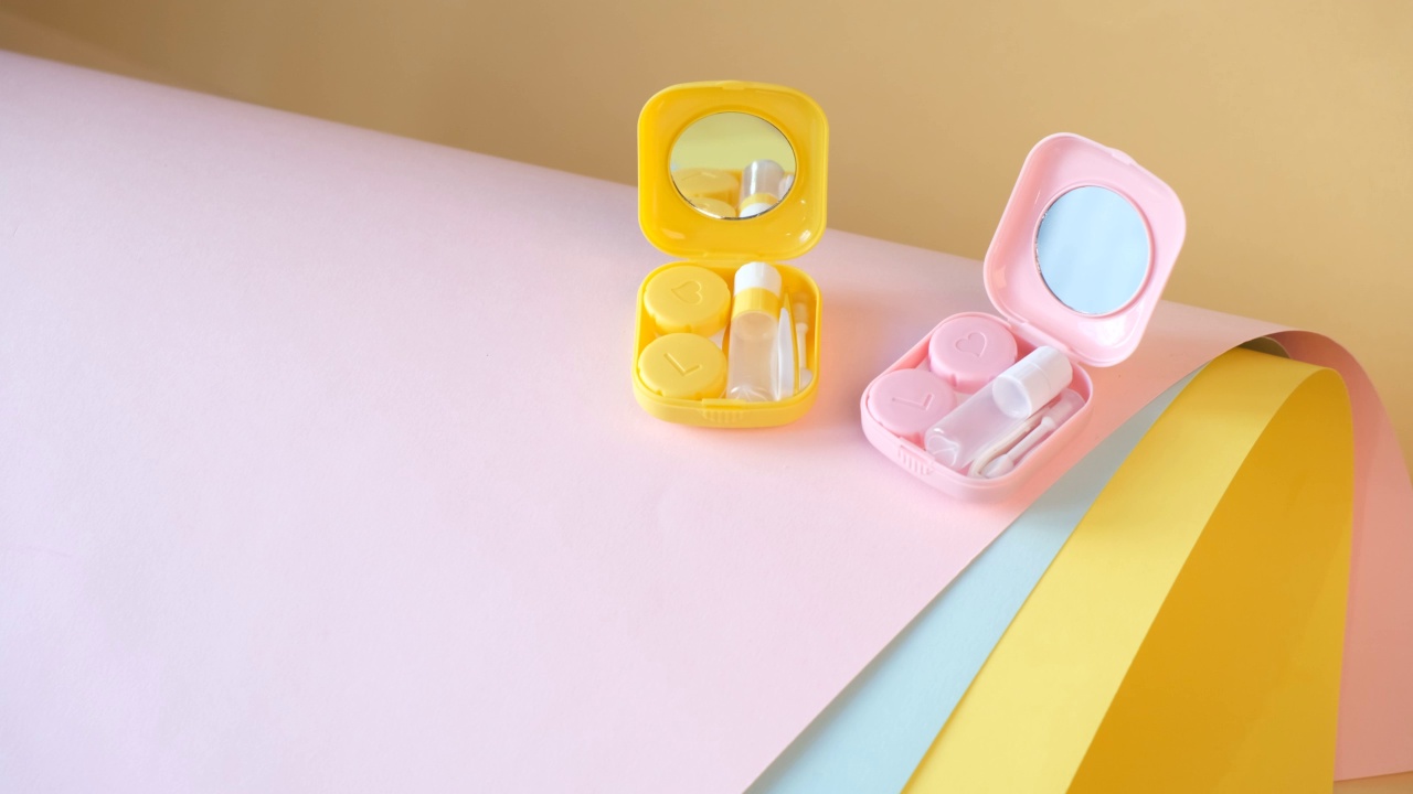 隐形眼镜装在可爱的粉色和黄色塑料容器上，背景是彩色的纸。每日镜片护理。视频下载