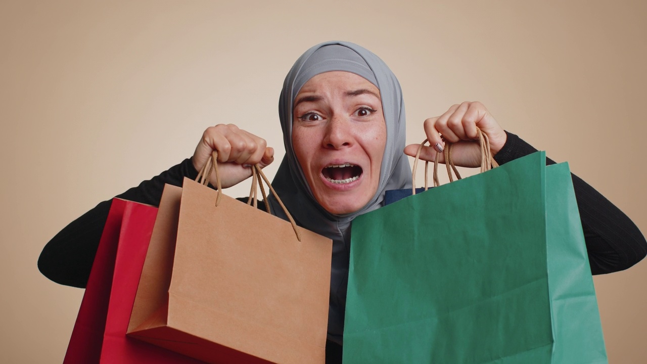 快乐的穆斯林妇女展示购物袋，广告节日折扣，惊讶于低价格视频素材