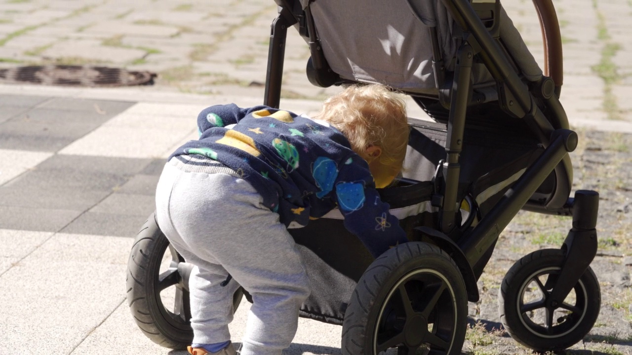 快乐的学步儿童在户外夏日公园玩婴儿车。视频下载