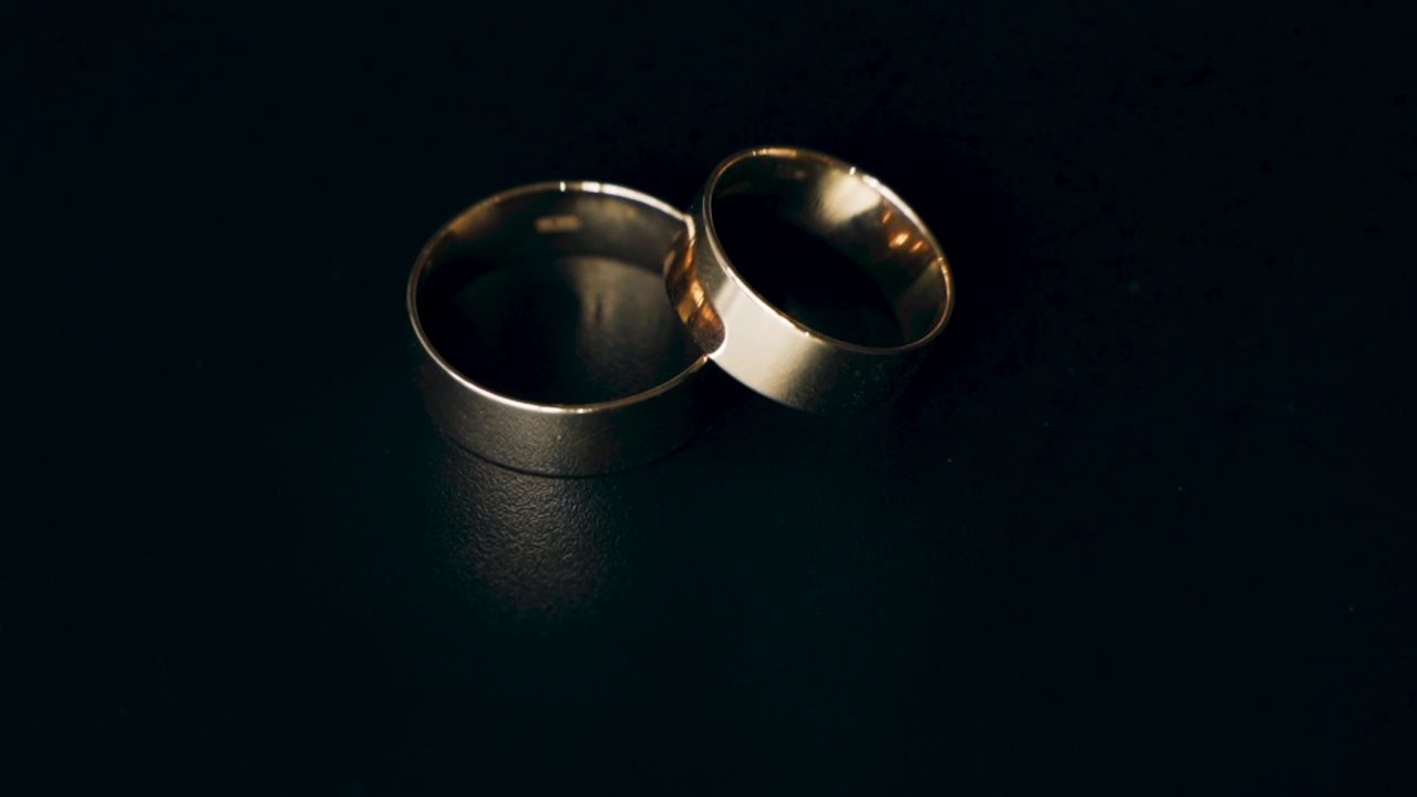 两枚金婚戒在黑色背景上旋转。视频下载