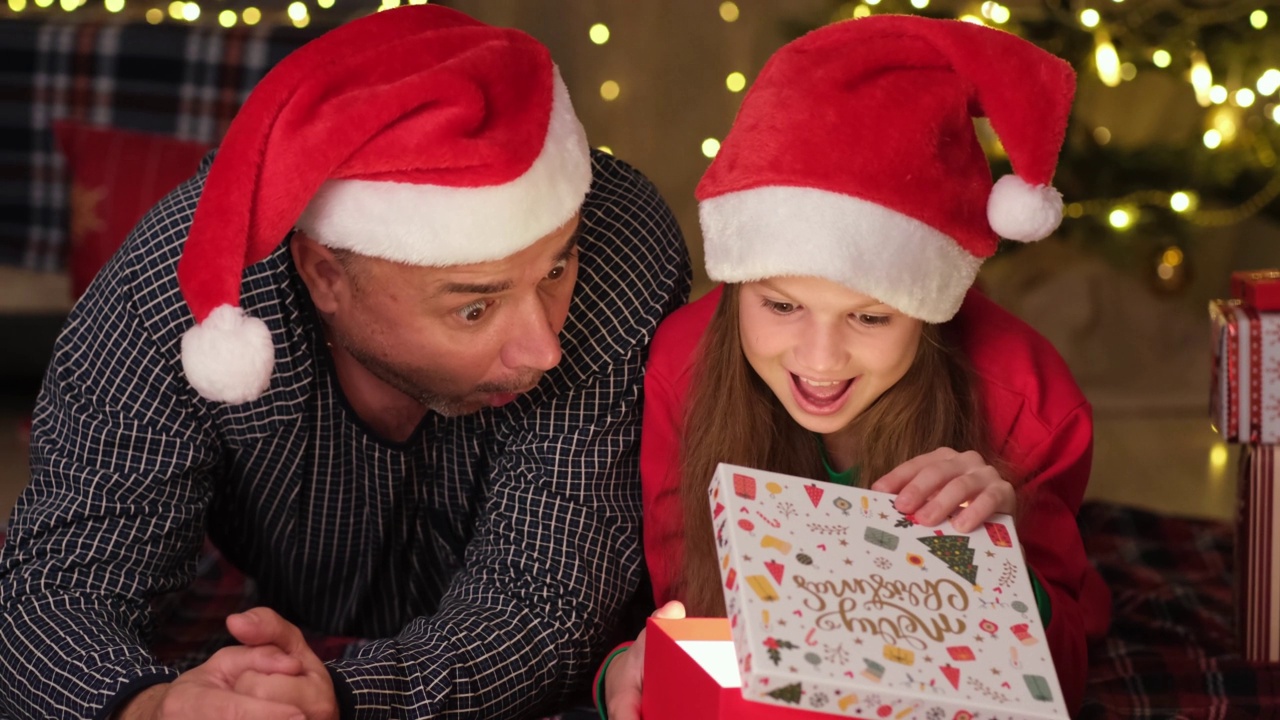 小女孩和戴着圣诞帽的爸爸在家里打开圣诞礼物视频素材