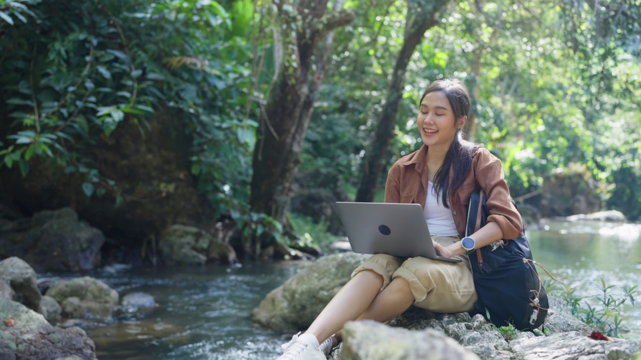 年轻的亚洲妇女在森林的位置使用电脑。视频下载