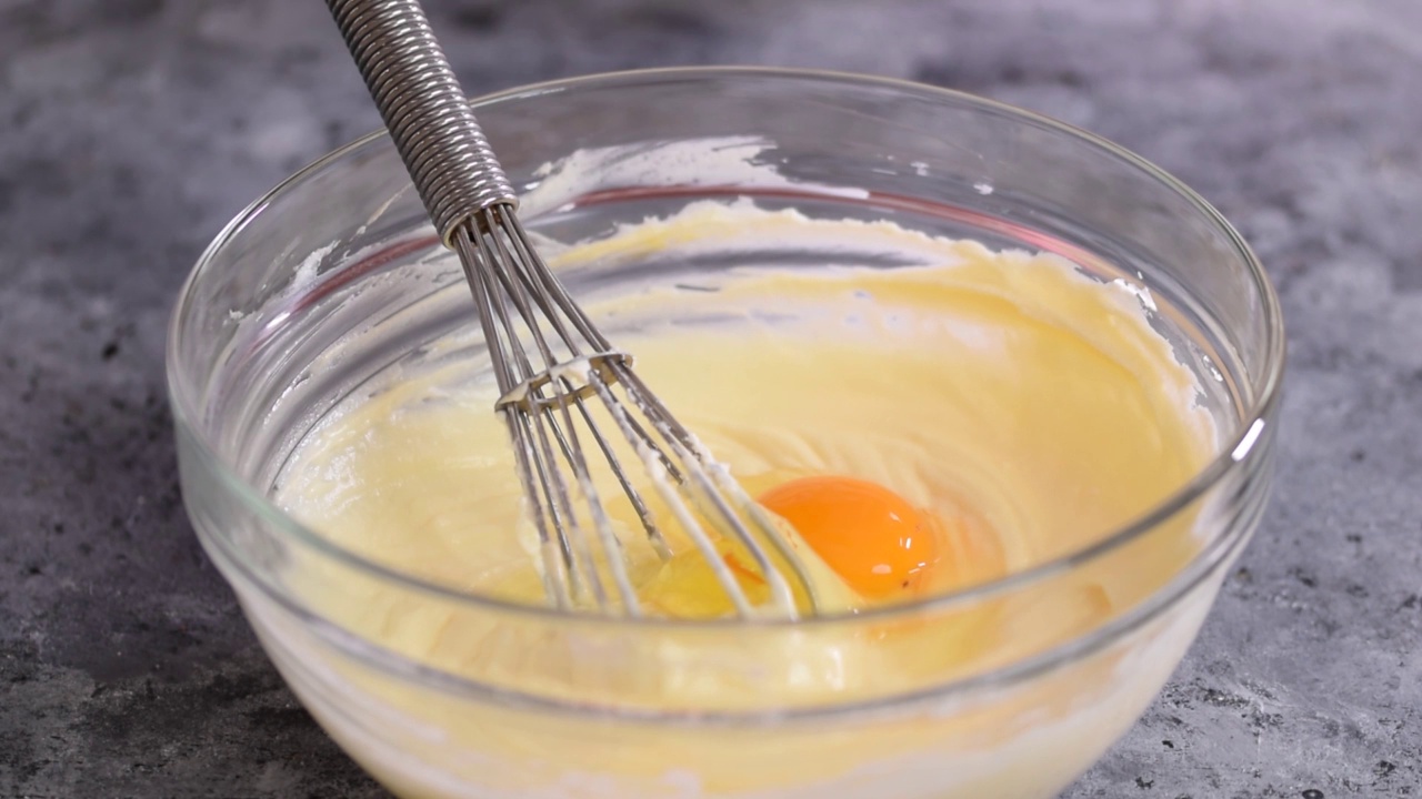 一位女士在奶油芝士混合物中加入了一个鸡蛋。一步一步做一个芝士蛋糕。视频下载