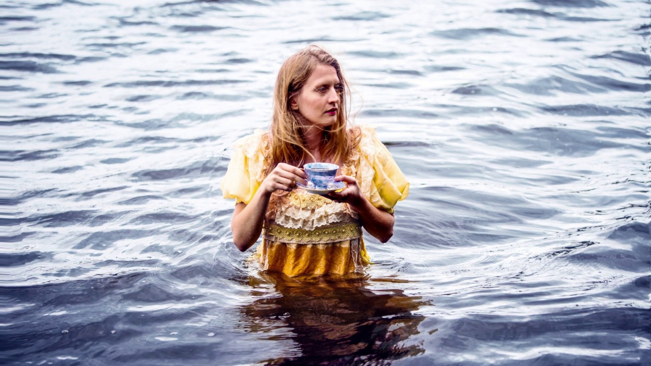 电影摄影的女人在黄色的衣服站在水里拿着一个茶杯视频下载