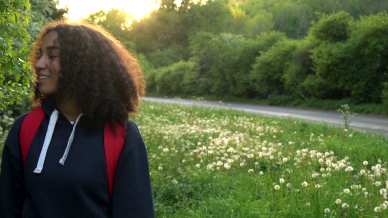 美丽快乐的混血儿非裔美国女孩，十几岁的女性，年轻的女人在日落或日出的时候背着红色的背包在乡下徒步旅行视频素材
