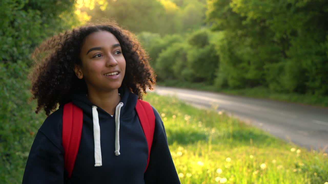 美丽快乐的混合种族非裔美国女孩，青少年，女性，年轻的女人在日落或日出时在农村徒步旅行红色背包视频素材
