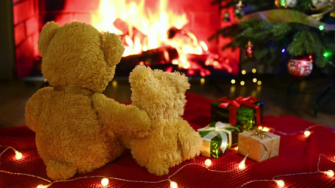 在壁炉、礼物和圣诞树的背景下，一对泰迪熊坐在一条针织毯子上相互拥抱。视频下载
