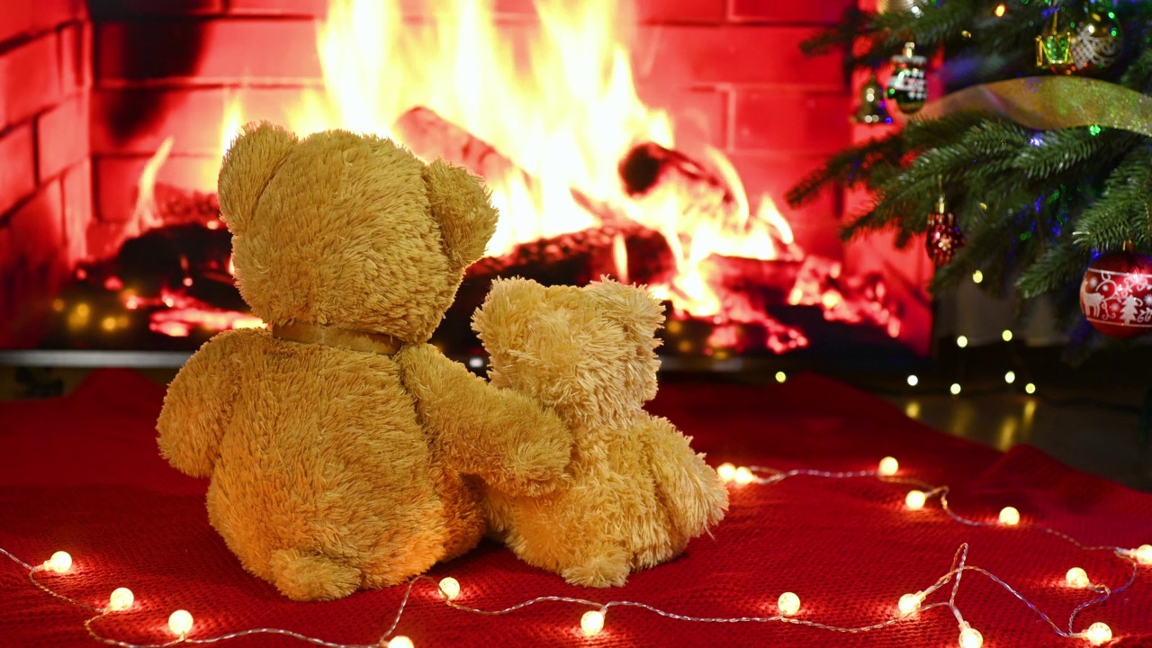 在壁炉、圣诞彩灯和圣诞树的背景下，一对泰迪熊坐在针织毯子上相互拥抱。视频下载