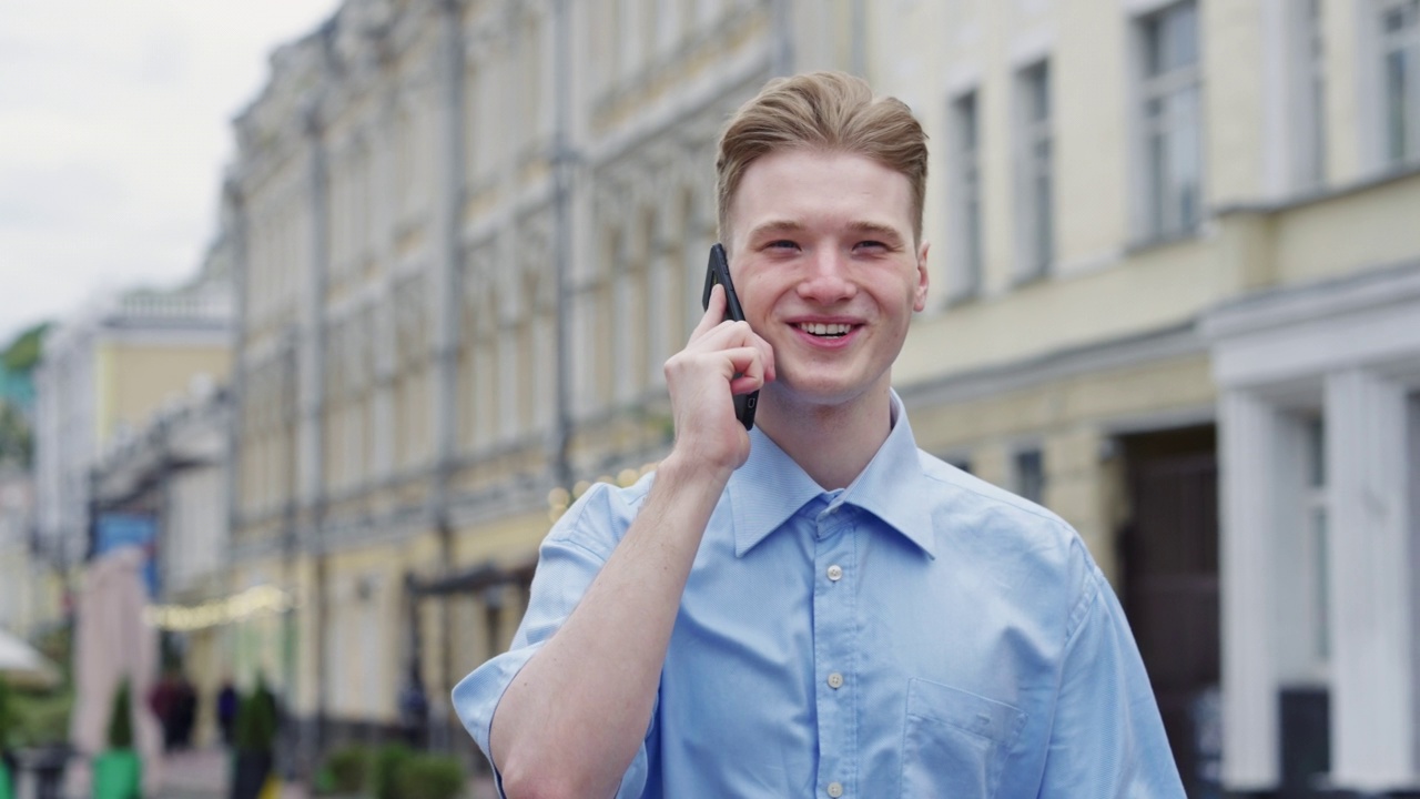 快乐的年轻金发男子在城市散步时打电话视频素材