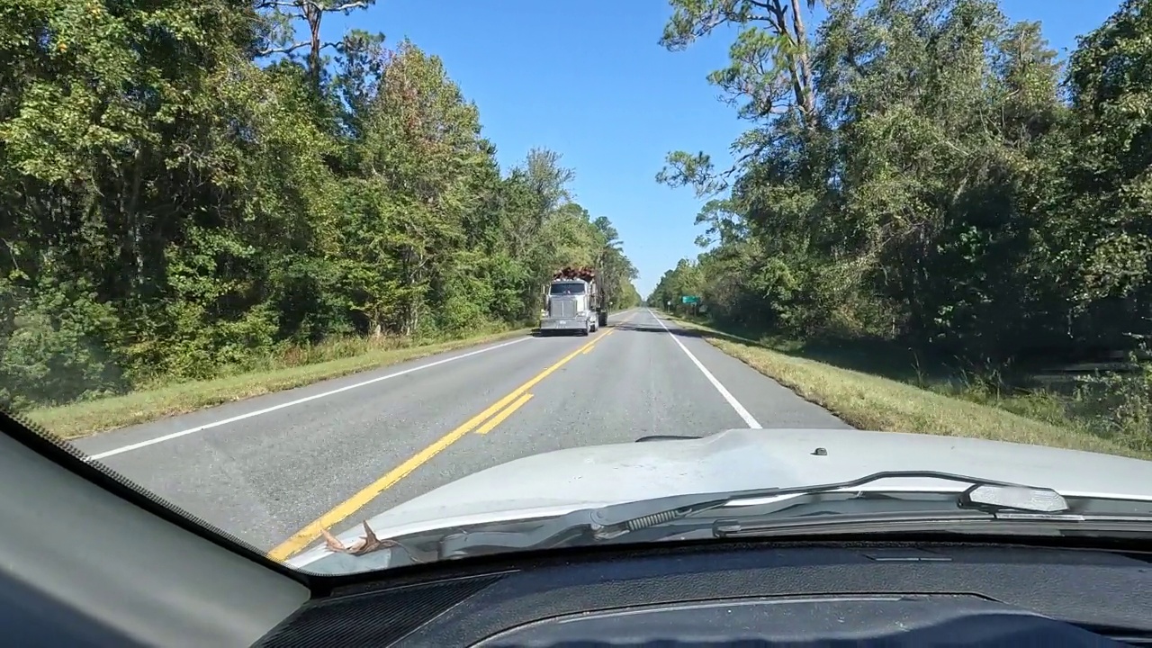 司机的视角，阳光明媚，荒凉的农村道路，单半卡车拉拖车与长松木从相反的方向视频下载